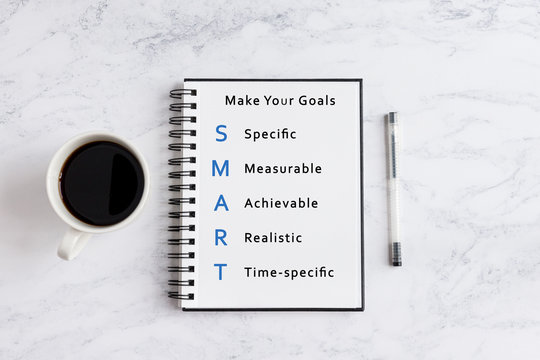 SMART goals writing on notebook. Notebook on desk with coffee cup and a pen.