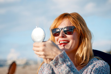Attractive young woman refreshing her makeup lipstick by holding a handheld mirror powder box on a sunny day © Cagkan