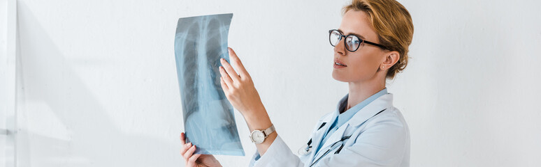 Obraz premium panoramic shot of attractive doctor in glasses looking at x-ray in clinic