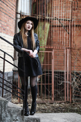 Young beautiful girl in a hat and with a dark make-up outside. Girl in the Gothic style on the street. A girl walks down the city street in a leather waistcoat with a phone.