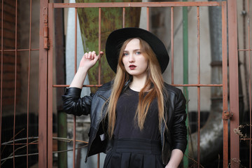 A girl walks down the city street in a leather waistcoat with a phone. Young beautiful girl in a hat and with a dark make-up outside. Girl in the Gothic style on street.