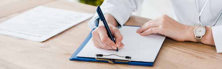 panoramic shot of doctor writing diagnosis on wooden table