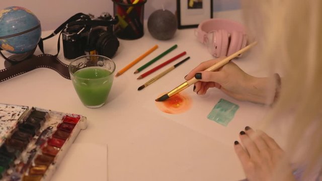 Close up student painting in watercolors using a paintbrush on watercolors paper. Study design tutorial animator illustrator work freelance session art home studio loft