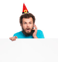 Crazy bearded Man with funny Curly Hair in Christmas hat showing empty blank signboard with copy space. Surprised guy in Santa hat peeking out from behind big white banner isolated on white background