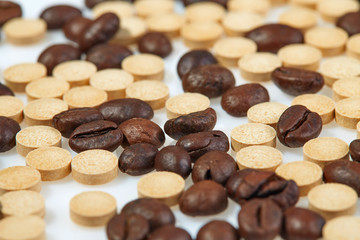 Coffee beans mixed with caffeine tablets are scattered on a light surface. Horizontal