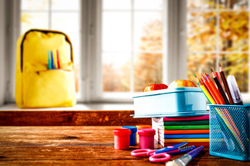 Schoolbags background with some school supplies on wooden desk top and a windowsill with white window autumn view. Empty space for product and decoration.