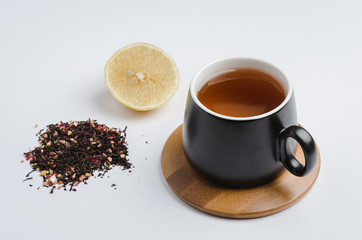 fruit tea in a black mug on a bamboo support, lemon segment and dried tea isolated on white background