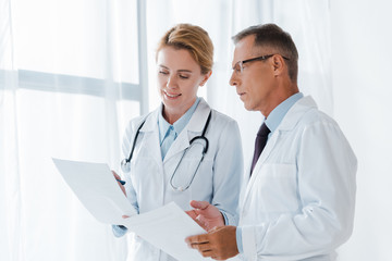 cheerful doctor holding paper near handsome coworker in glasses