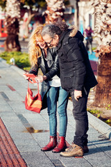 Caucasian adult hipster couple at 40s smiling and taking a selfie on the street on a sunny winter...
