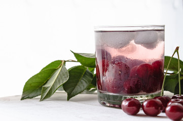 Fresh cherry cocktail with ice on a white wooden background. Fresh summer cocktail with cherries and ice cubes.