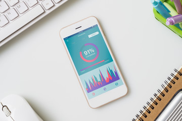 Top view of office desk table with graph chart on mock up smartphone on white desk table. Business management reports via mobile application concepts ideas. Mobk up mobile phone.