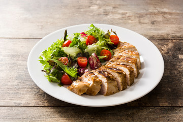 Grilled chicken breast with vegetables on a plate on wooden table