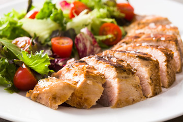Grilled chicken breast with vegetables on a plate on wooden table. Close up