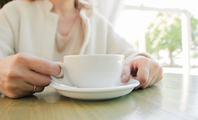 Cup of fresh cappuccino coffee in female hands on the table in summer cafe