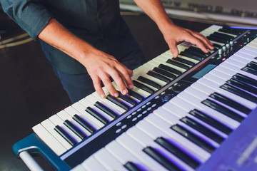 Man playing electronic musical keyboard synthesizer by hands on white and black keys in recording studio.