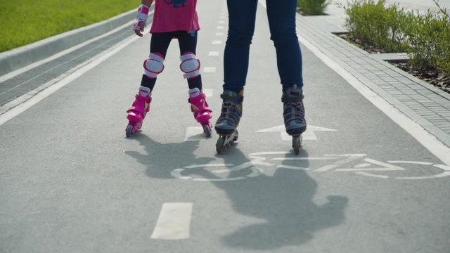 Mother with the Daughter Go On Roller Skates Outdoors. Woman and Little Girl Rollerblading on a Bicycle Lane in a City Park. Close Up. Slor Motion. Active Family Lifestyle Concept