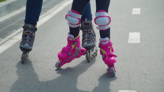Mother Teaching her Daughter Rollerblading. Close Up. Little Girl with Mother Roller Skating Outdoors. Slow Motion. Summer Family Activities Concept