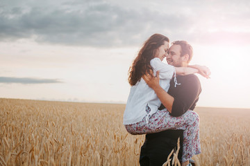 Loving couple in a wheat field hugs at sunset