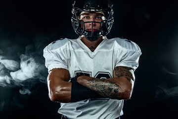 American football sportsman player in helmet on black background with smoke. Sport and motivation...