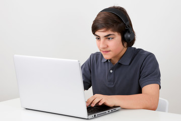 Gamer kid wears a wireless headphone and plays a computer game at his laptop computer