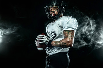 Fototapeta na wymiar American football sportsman player in helmet on black background with smoke. Sport and motivation wallpaper.