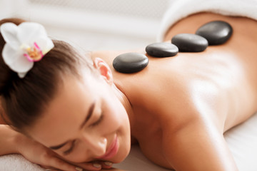 Fototapeta na wymiar Young woman enjoying hot stone massage at spa salon