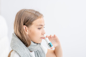 Sick girl with flu using nose spray at home