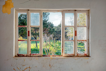 Vintage wooden window frame with broken glass looking through a green meadow field. of an Interior of a desolated house with dirty cracked wall. - obrazy, fototapety, plakaty