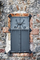Vintage window with black iron shutter and stone wall of an antique house