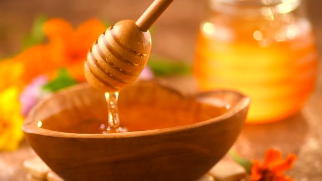 Honey dripping from honey dipper in wooden bowl. Healthy organic thick honey closeup. Slow motion. 3840X2160 4K UHD video footage