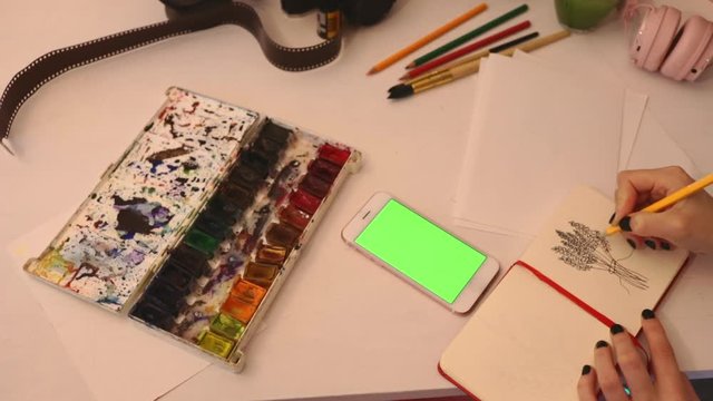 close up woman painting from smartphone on table with art objects watercolor brush studio home loft 5g green screen chroma key social technology media study design tutorial illustrator work freelance