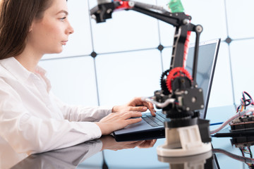 A young woman writes an algorithm for the robot arm. Science Research Laboratory for Robotic Arm Model. Computer Laboratory