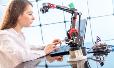 A young woman writes an algorithm for the robot arm. Science Research Laboratory for Robotic Arm Model. Computer Laboratory