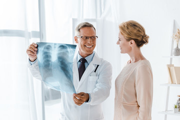 happy doctor looking at attractive patient and holding x-ray in clinic