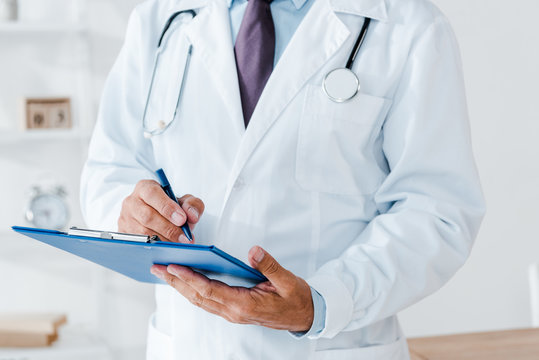 cropped view of doctor in white coat holding clipboard and writing diagnosis