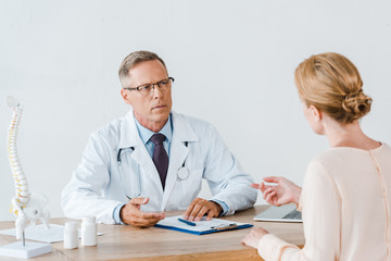 selective focus of doctor in glasses looking at woman gesturing while sitting near table