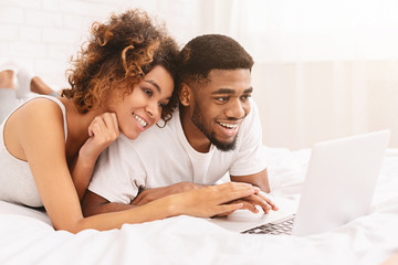 Young black couple lying on bed and using laptop