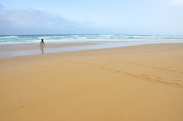 Fototapeta na wymiar Girl Wearing a Dress Walking by a Long Sand Beach in Fuerteventura, Canary Islands