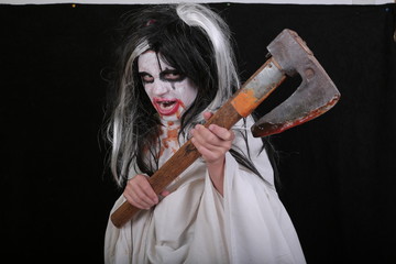 Halloween horror concept. Cute little scary girl in monster zombie costume with blood axe on black...