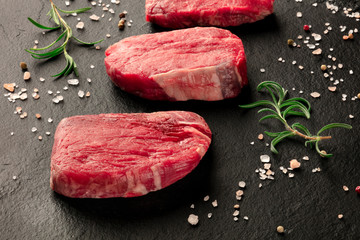 Raw beef steaks, fillet or sirloin, with salt, pepper and rosemary on a black background