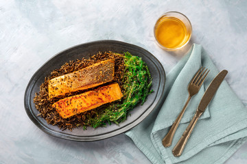 Grilled salmon with sesame seeds, wakame seaweed and wild rice, shot from the top with a glass of white wine