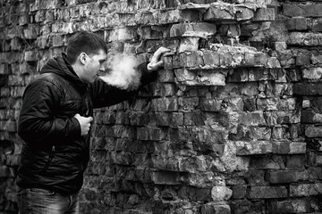 Vape man. Young caucasian white guy in black jacket smoking and letting off steam from an...