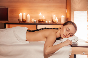 Obraz na płótnie Canvas Beautiful young woman enjoying relaxing treatments the stone therapy at the spa salon by candlelight. The concept of relaxing and rejuvenating procedures