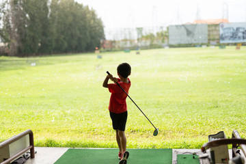 Young asian boy is practicing his golf swing at the golf driving range.