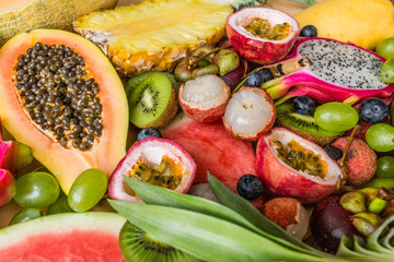 Fresh exotic fruits and tropical palm leaves on pastel orange background - papaya, mango, pineapple, passion fruit, dragon fruit, grapes, lichee, kiwi, melon. Mockup, flat lay, overhead. Top view.