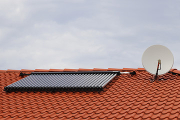 Vacuum collectors - solar water heating system on red roof of the house with satellite.