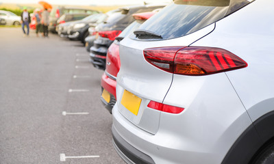 Closeup of rear, back side of white car with  other cars parking in outdoor parking area in bright sunny day. 