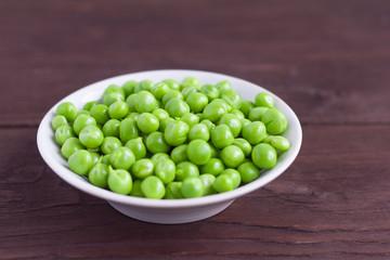 young green peas in white saucer on wooden background