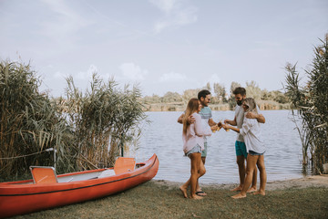 Obraz premium Group of friends with cider bottles standing by the boat near the beautiful lake and having fun