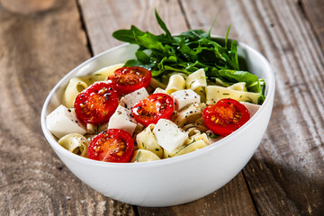 Pasta with tomatoes and white cheese on wooden table